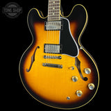A double-cutaway electric guitar with a classic sunburst finish, featuring a bright yellow-orange center fading to black around the edges. It has a black pickguard, chrome hardware, and gold-toned control knobs, shown against a solid black background with a Tone Shop watermark in the top left corner.