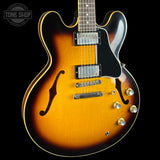 A close-up of a Sunburst electric guitar body with a black pickguard, chrome hardware, and gold control knobs, set against a solid black background with a Tone Shop watermark in the top left corner.