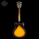 A classic six-string electric guitar shown from the back, featuring a glossy sunburst finish that transitions from bright orange in the center to black at the edges. The neck is made of a warm brown wood, and the headstock is equipped with six silver tuning pegs.