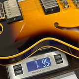 Close-up of a sunburst electric guitar resting on a digital scale showing a weight of 7.95 lbs.