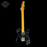 Black electric guitar with a yellow neck on a black background, featuring 'Tone Shop' branding.