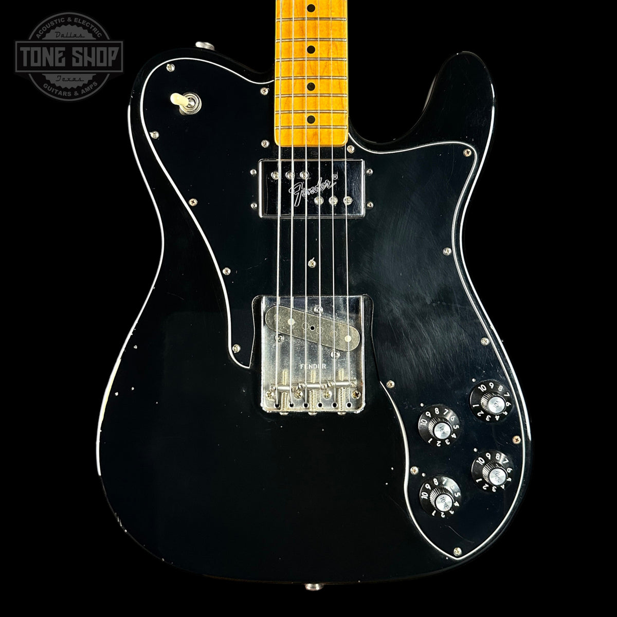 Black electric guitar with a clear body on a black background, featuring the Tone Shop logo.