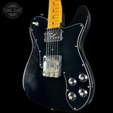 Black electric guitar with a yellow pickguard on a black background, featuring 'Tone Shop' branding.
