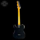 Black electric guitar with a yellow pickguard on a black background, featuring 'Tone Shop' branding.