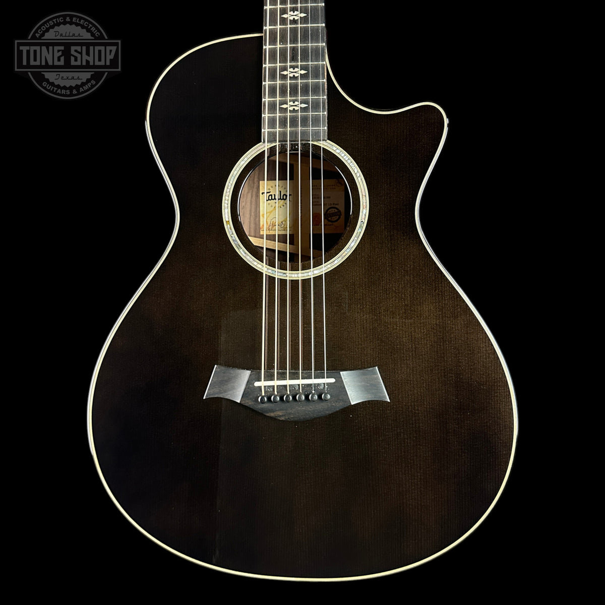 Acoustic guitar with a dark brown finish on a black background, featuring the Tone Shop logo.