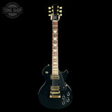 Black electric guitar with gold hardware on a black background, featuring 'Tone Shop' logo.