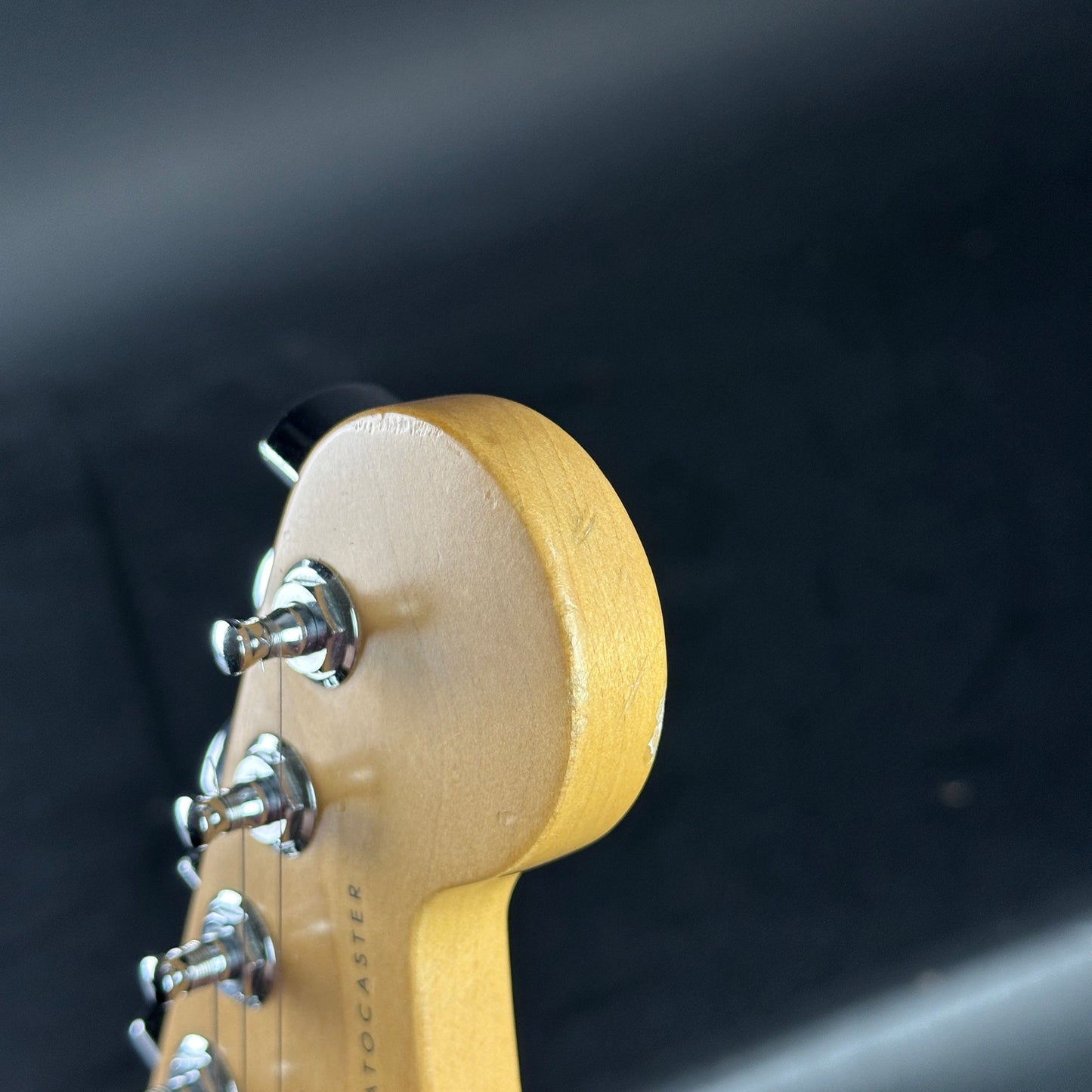 Close-up of a guitar headstock with tuning pegs on a dark background