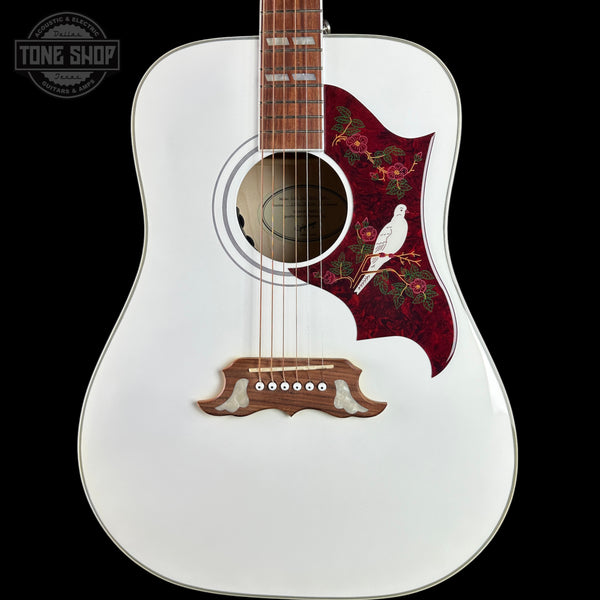 A white acoustic guitar with a decorative red pickguard featuring floral patterns and a white bird, shown against a solid black background.