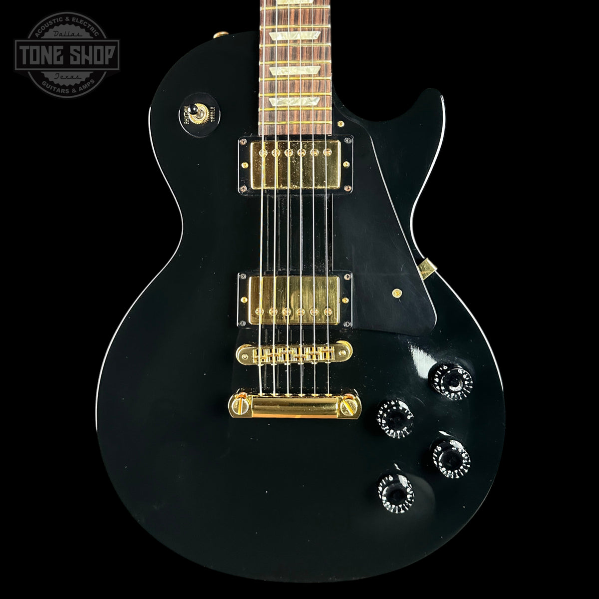 Black electric guitar with gold hardware on a black background, featuring 'Tone Shop' logo.