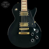 Black electric guitar with gold hardware on a black background, featuring 'Tone Shop' logo.