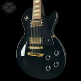 Black electric guitar with gold hardware on a black background, featuring 'Tone Shop' logo.