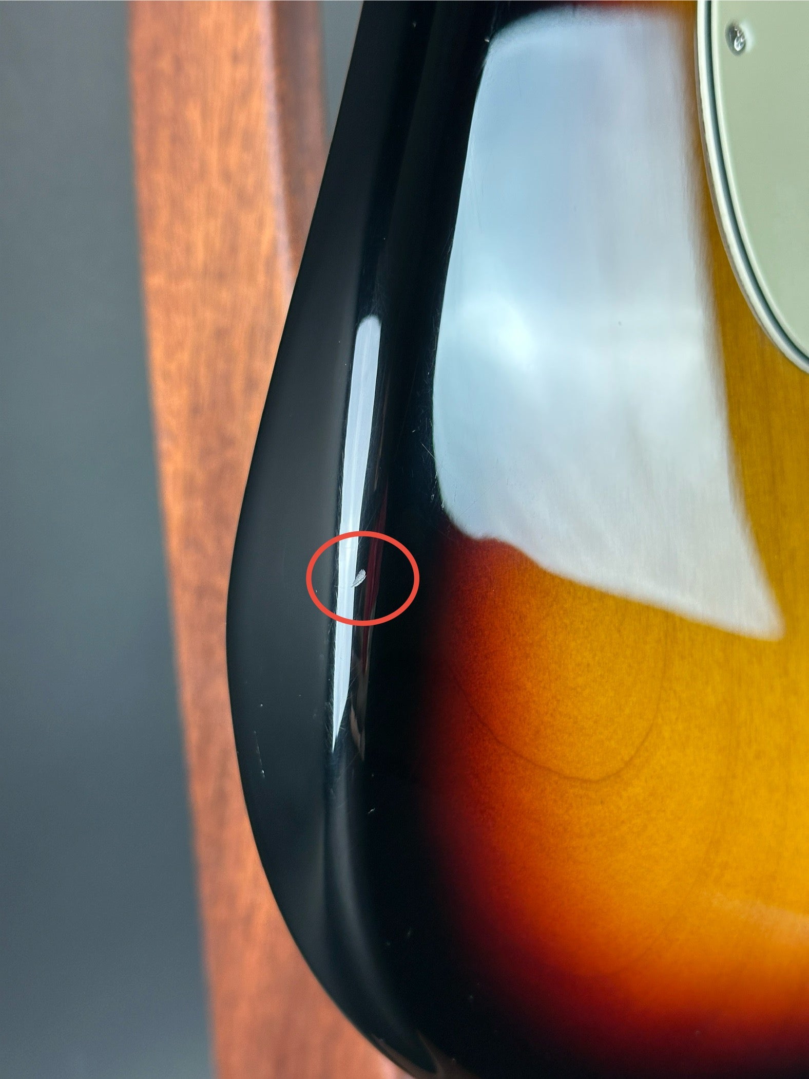 Close-up of a guitar with a red circle highlighting a small scratch on the black part.