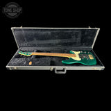 Green bass guitar in a black case with 'Tone Shop' logo.