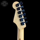 Close-up rear view of a guitar headstock with a natural wood finish and dark blue tuning pegs, shown against a black background with a Tone Shop watermark in the upper left.