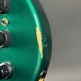 Close-up of a green guitar with visible wear and a gold label on a gray background