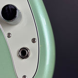 Close-up of an electric guitar body showing a metallic mint green finish, a cream pickguard, and chrome hardware against a dark gray background.