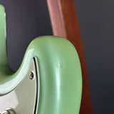 Close-up of a glossy mint green electric guitar body with a white pickguard and silver hardware, set against a dark gray background with a blurred brown wooden element.