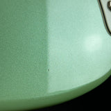 Close-up of a mint green metallic guitar body with a satin finish and a small visible defect near the center.
