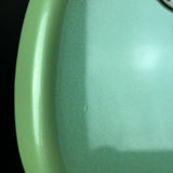 A close-up of a glossy mint green curved surface, likely part of a vehicle or motorcycle body panel, showing a fine metallic texture against a black background.