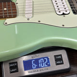 A mint green electric guitar body shown close-up with a digital scale underneath to display its weight, which reads 6 lbs 2 oz.