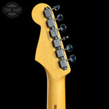 Close-up of the headstock of a Fender Stratocaster electric guitar in a natural maple wood finish, showing the six tuning pegs and brand name, set against a solid black background.