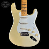 A classic Fender Stratocaster electric guitar in a cream finish, featuring a white pickguard, gold-toned hardware, and a maple neck, shown against a solid black background.