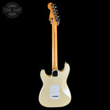 Fender Stratocaster electric guitar shown from the back, featuring a cream-colored body, maple neck, and gold-toned tailpiece, photographed against a solid black background.