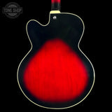 Close-up of the back of an electric guitar body with a glossy black finish, a bright red sunburst center, and a cream-colored binding against a black background.