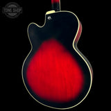 Close-up of the back of an electric guitar with a glossy red sunburst finish, cream binding, and a dark neck visible at the top, shown against a black background with a Tone Shop watermark in the upper left.