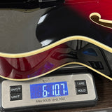 Close-up of a red and black electric guitar body resting on a digital scale displaying 6.107 oz.
