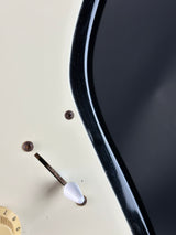 Close-up of a guitar with a black pickguard, white pickguard, and tuning pegs.