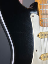 Close-up of a black electric guitar with visible wear on the body.