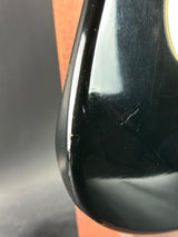 Close-up of a black car fender with a scratch on a wooden surface.