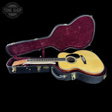 Acoustic guitar in an open case with a visible brand logo on a black background