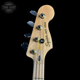 Close-up of a Fender Squier Jazz Bass headstock on a black background with 'Tone Shop' logo.