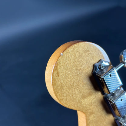 Close-up of a wooden guitar headstock with tuning pegs against a dark background
