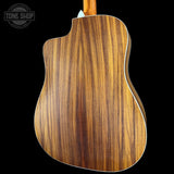 Close-up of the back of an acoustic-electric guitar showing a rich wood grain finish, with a white binding edge and a Tone Shop logo watermark in the top left corner.