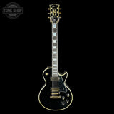 Electric guitar with a black finish and gold hardware on a black background, featuring the Tone Shop logo.