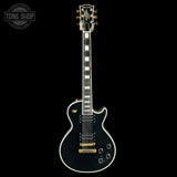 Black electric guitar with gold hardware on a black background, featuring the Tone Shop logo.