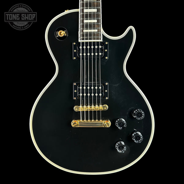 Black electric guitar with gold hardware on a black background, featuring 'Tone Shop' logo.