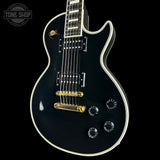 Black electric guitar with gold hardware on a black background, featuring 'Tone Shop' branding.