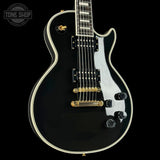 Black electric guitar with gold hardware on a black background, featuring 'Tone Shop' logo.