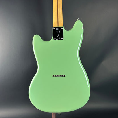 Green electric guitar with a wooden neck against a dark background