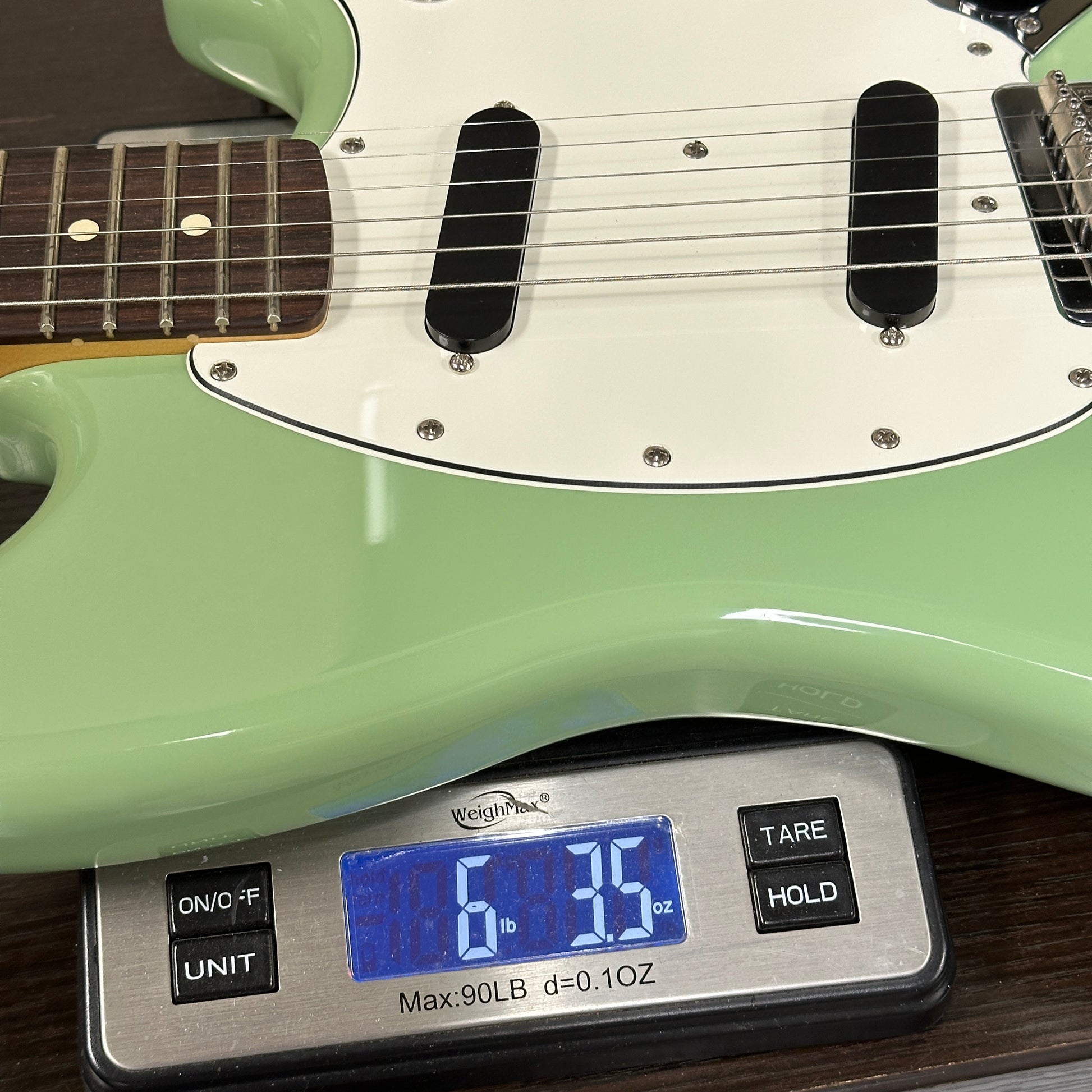 Green electric guitar on a digital scale displaying weight.