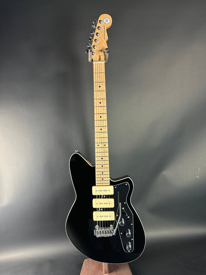 Black electric guitar with a maple neck on a reflective gray surface