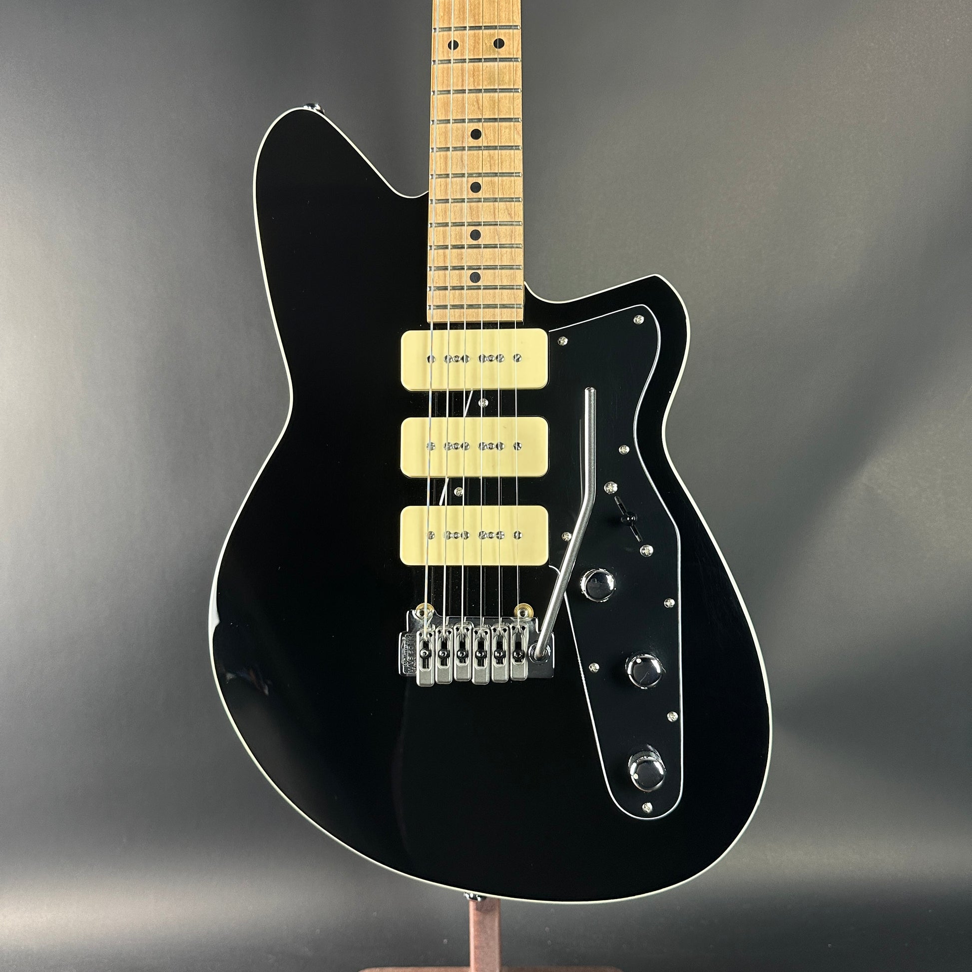 Black electric guitar with a wooden neck on a dark gray background