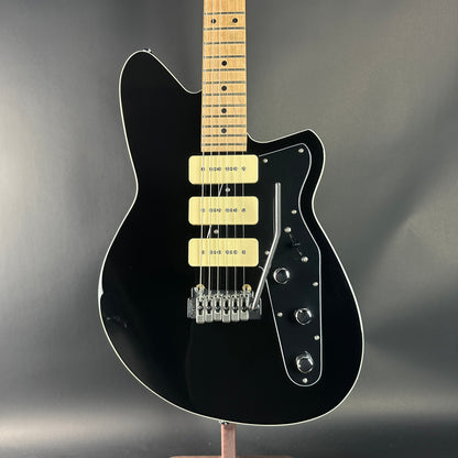 Black electric guitar with a wooden neck on a dark gray background