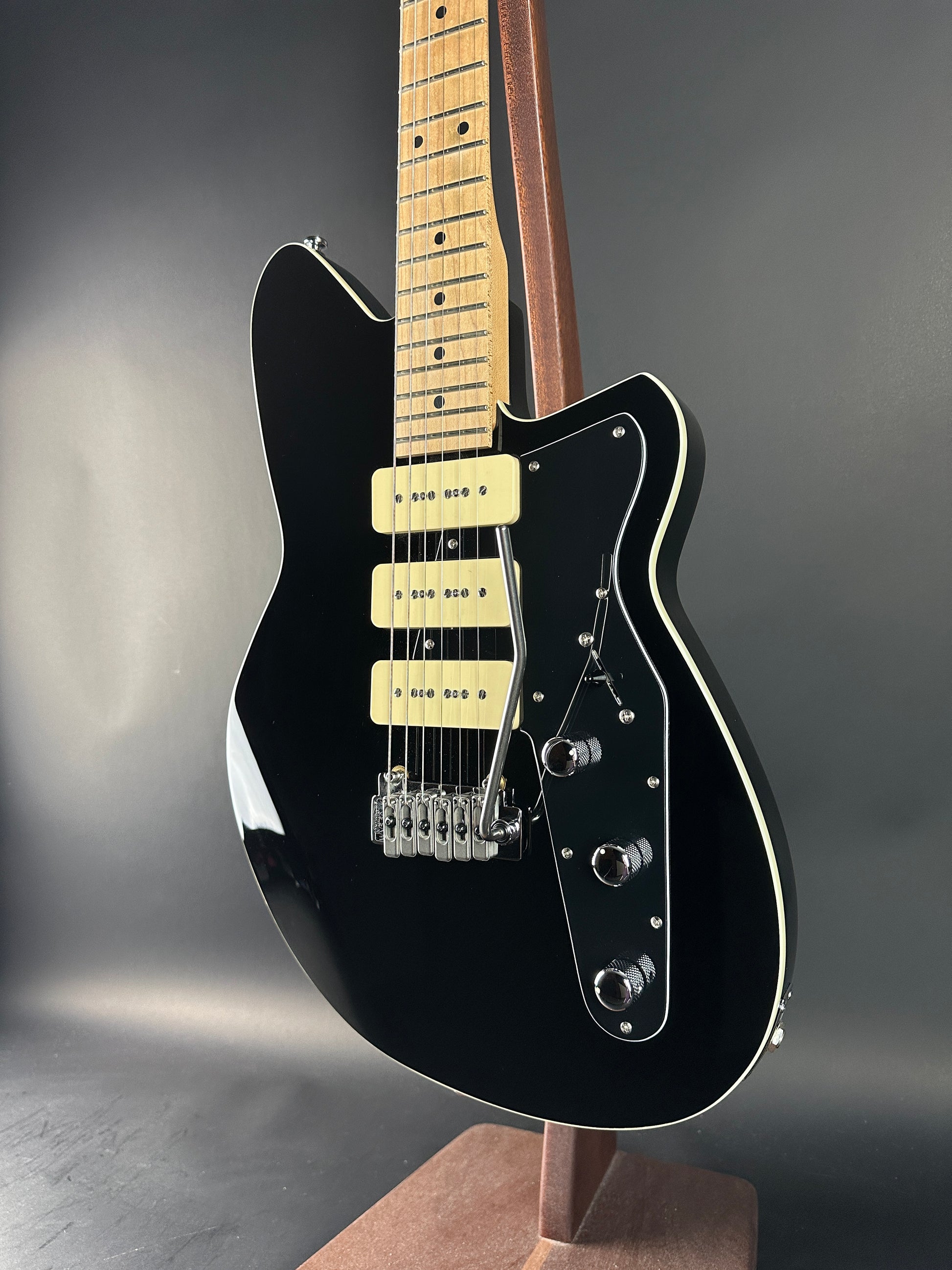 Black electric guitar with a wooden fretboard on a dark background