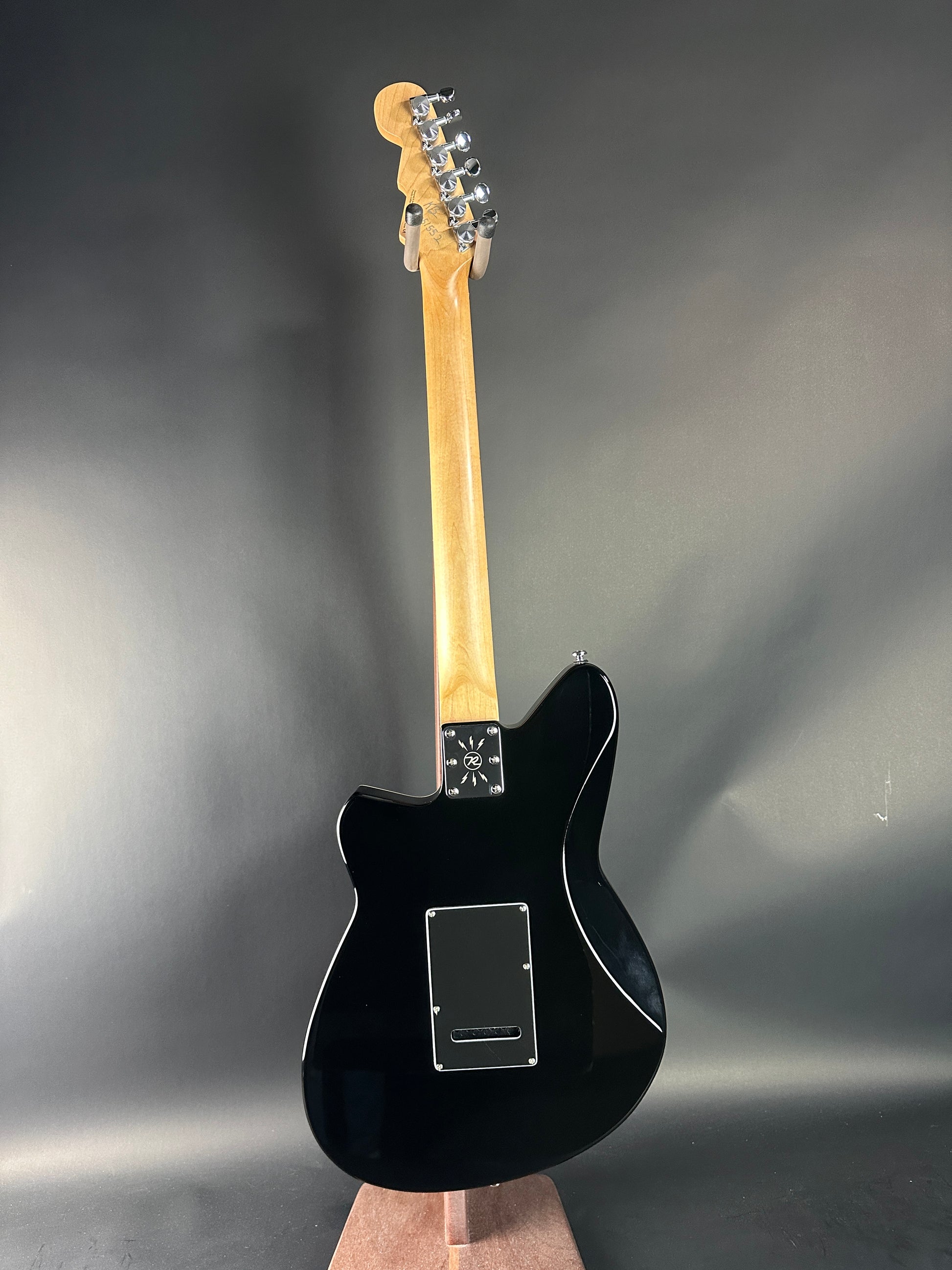 Black electric guitar with a wooden neck on a reflective gray surface