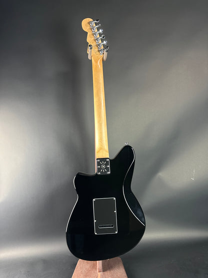 Black electric guitar with a wooden neck on a reflective gray surface